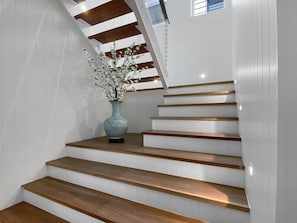 Eine Treppe mit Holzbodenstufen und weißen Wänden, eine Vase mit Blumen und ein Oberlicht.