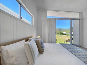 Quarto com uma cama grande, vista para um jardim e porta deslizante para área externa.