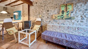 A rustic interior with exposed wooden beams, a stone wall, a sofa, and a dining area with chairs and a table. - San Francisco 58  (Santo Domingo de la Calzada)
