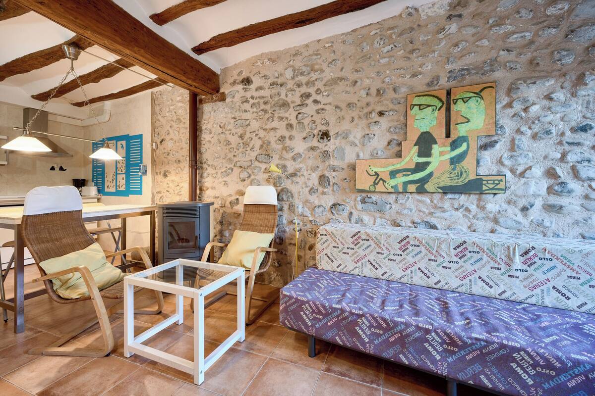 Un intérieur rustique avec des poutres apparentes, un mur en pierre, un canapé et un coin repas comprenant des chaises et une table.