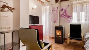 A cozy room with a wooden chair, a red dresser, a television, a heater, and a bed with a checkered blanket. - San Francisco 58  (Santo Domingo de la Calzada)