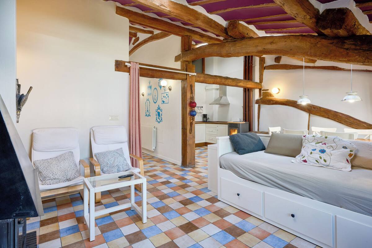 Une pièce chaleureuse avec un sol à carreaux, un lit avec des oreillers, un canapé blanc et une petite table.