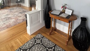 Ein Wohnzimmer mit Holzboden, einem gemusterten Teppich, einem runden Spiegel und einem kleinen Tisch mit einer Vase und einem gerahmten Bild.