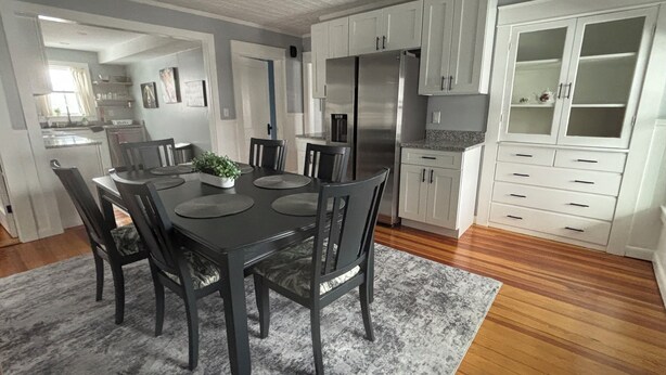 Eine moderne Küche mit weißen Schränken, einem Edelstahlkühlschrank und einem Essbereich mit einem dunkelholztisch und Stühlen.