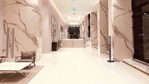 Una hall d'hotel moderna con pareti in marmo, una scalinata centrale e un'area salotto con un tavolo e sedie.