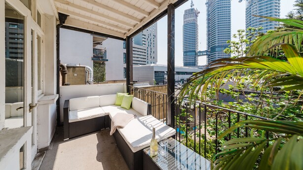 A balcony with a white sofa, a glass table, and a bottle of wine. In the background, there are tall buildings and a construction crane. - NEW: Luxurious 2 bed 2 bath, E14 Flat (Greater London)