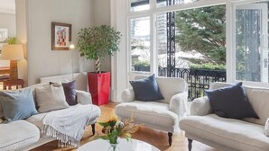 A spacious living room with a white sofa set, a coffee table, and a large window offering a view of the outdoors. - NEW: Luxurious 2 bed 2 bath, E14 Flat (Greater London)