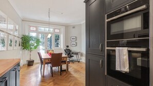 A modern kitchen with dark cabinetry, a wooden dining table, and a large window. - NEW: Luxurious 2 bed 2 bath, E14 Flat (Greater London)