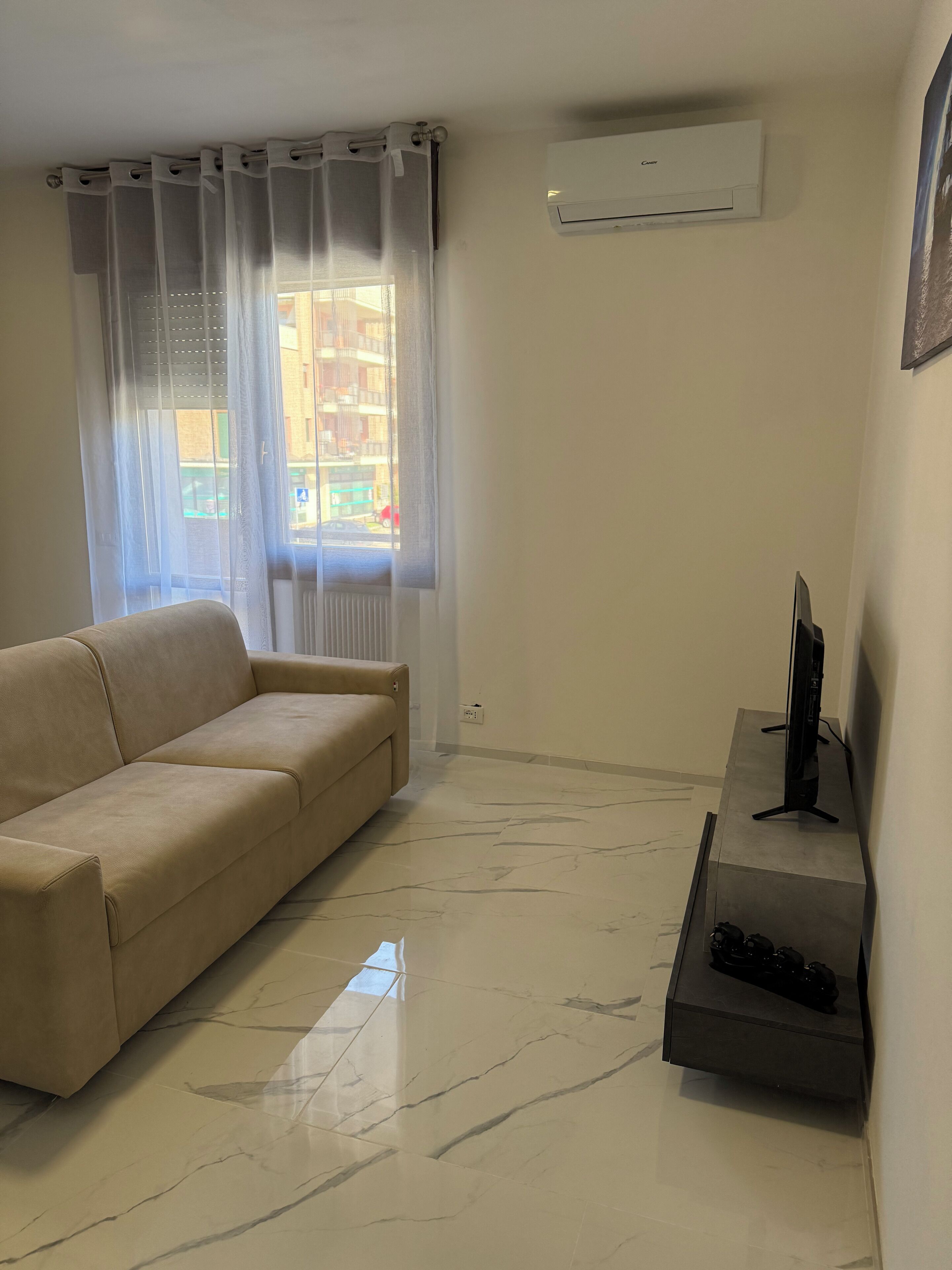 Een woonkamer met een beige bank, een flatscreen televisie op een standaard en een airconditioning aan de muur.