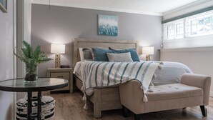 Une chambre à coucher avec un lit, des tables de chevet, une chaise, une petite table avec une plante et une fenêtre.