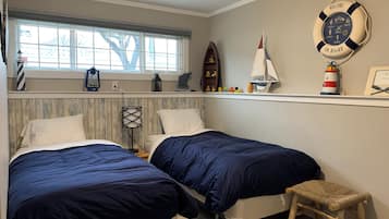 Ein Schlafzimmer mit zwei Betten, einem Fenster, einem Regal mit maritimer Dekoration und einem kleinen Holzschemel.