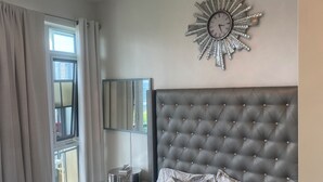 A bedroom with a tufted headboard, a decorative wall clock, and a bedside table with a lamp. - CityView Toronto CN Tower Waterfront (Toronto)