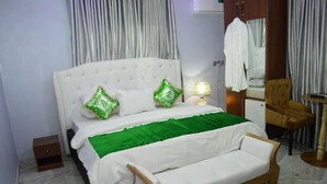 Un lit bien fait, avec une couverture verte et deux oreillers, une lampe de chevet, une chaise et une petite table.