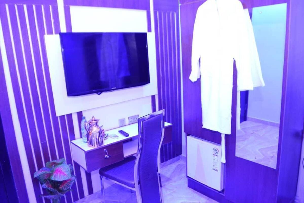 Une chambre d’hôtel équipée d’une télévision à écran plat, d’un bureau avec une chaise, d’un miroir et d’une robe blanche accrochée au mur.