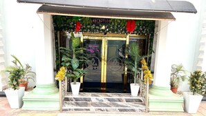 L’entrée d’un hôtel, avec un comptoir d’accueil, une pancarte « Bienvenue » et des plantes en pot.