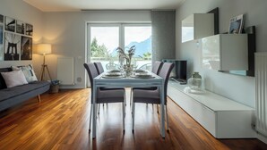 A modern living room with a dining table set for four, a sofa, and a view of mountains through large windows.