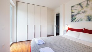 A modern hotel room with a large bed, white wardrobe, and a painting on the wall.