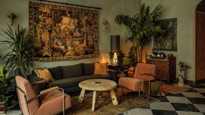 Uma sala de estar com uma grande tapeçaria, um sofá, uma mesa de centro e um candelabro.