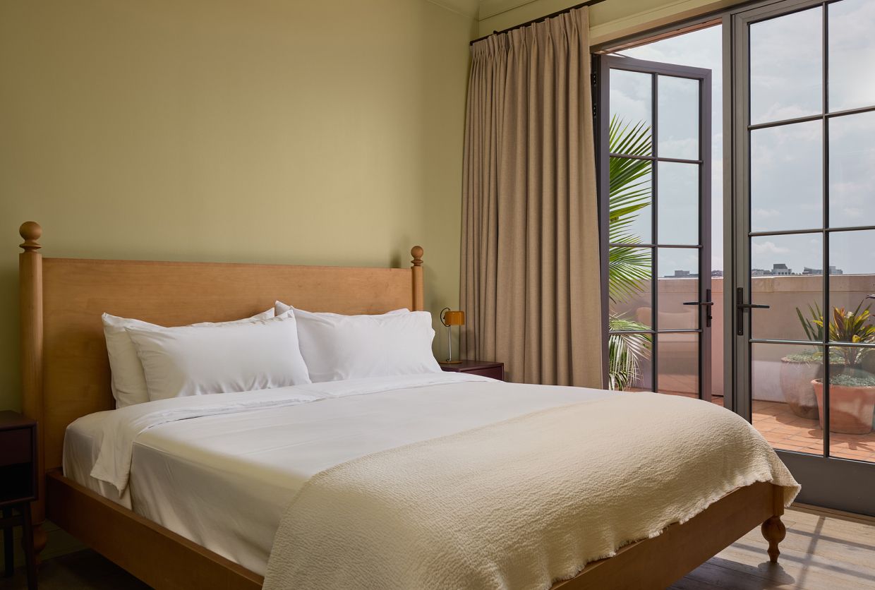 Een hotelkamer met een houten bed, een nachtkastje, een raam met gordijnen en uitzicht op de omgeving.