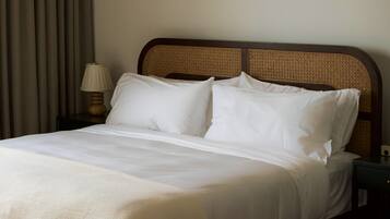 A bed with a headboard, pillows, a blanket, a lamp, and a curtain.