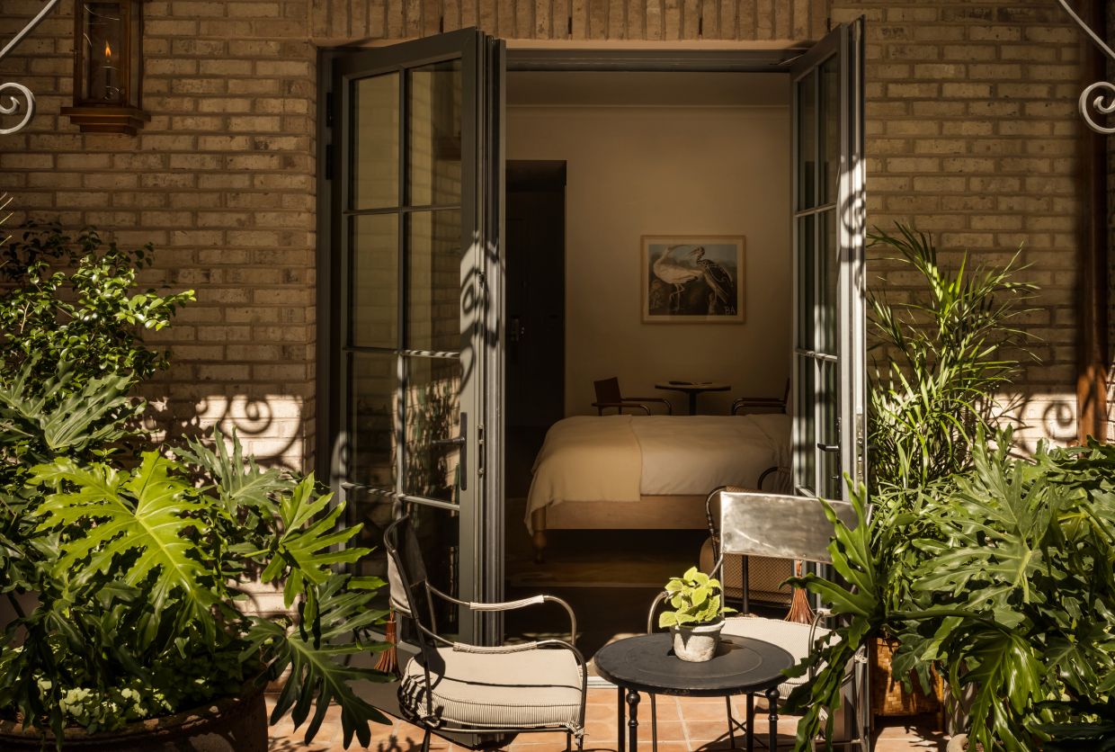 An open glass door leading to a bedroom with a bed and a painting on the wall.