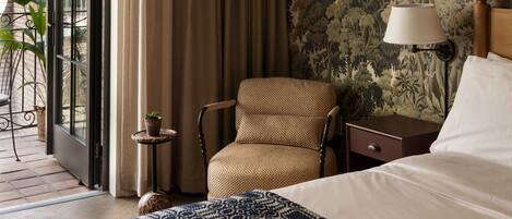 A hotel room with a bed, a chair, a nightstand, a lamp, and a view of the outdoors.