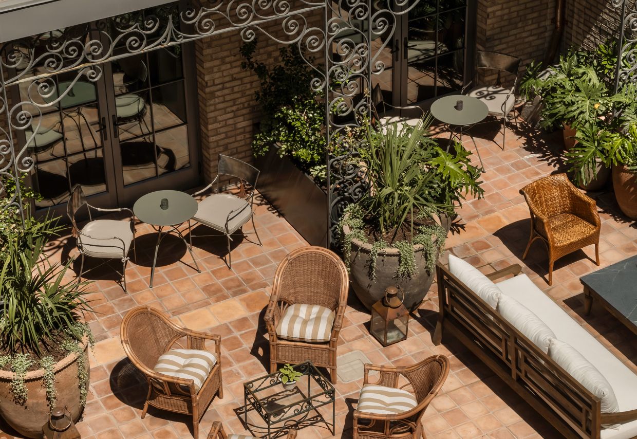 An outdoor patio with wicker furniture, potted plants, and a glass door leading to a room.