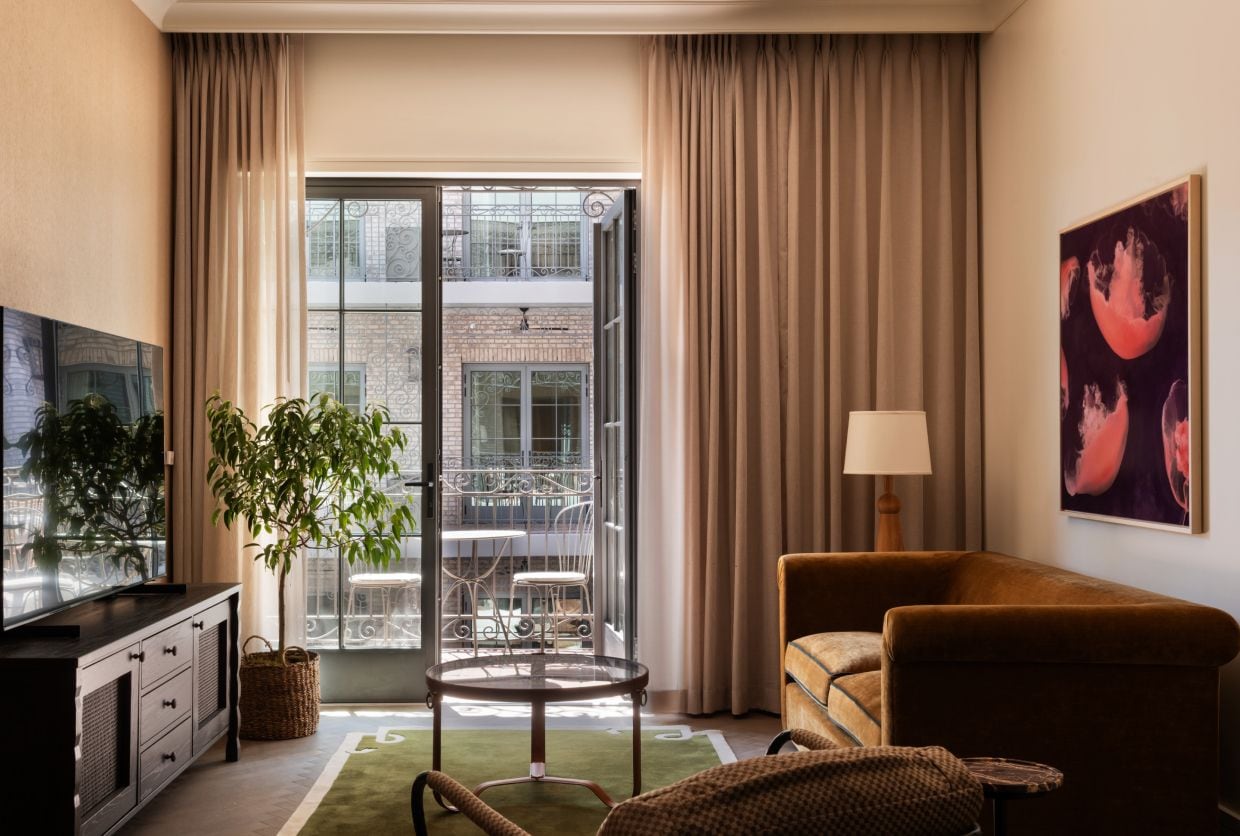 A hotel room with a television, a sofa, a table, a potted plant, and a view of the outside balcony.
