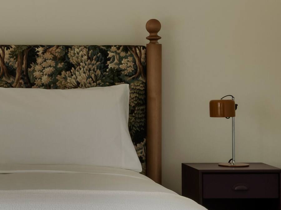 A neatly made bed with a headboard, a bedside lamp, and a nightstand with a drawer.