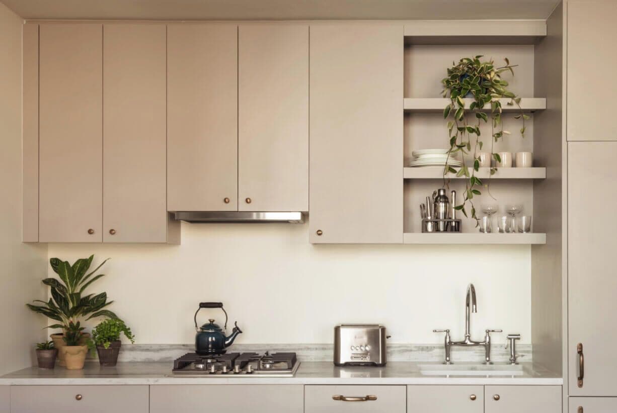 A kitchen with cabinets, a gas stove, a kettle, a toaster, a sink, and shelves with plants and kitchenware.