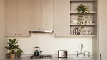 A kitchen with cabinets, a gas stove, a kettle, a toaster, a sink, and shelves with plants and kitchenware.