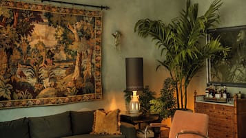 Una sala de estar con un tapiz grande, una araña, un sofá, una silla, una mesita y un aparador.