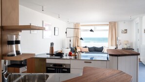 Eine moderne Küche mit einer großen Kochinsel, ein Essbereich mit Meerblick und eine gemütliche Sitzecke mit Kissen.