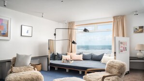 Ein modernes Zimmer mit einem Bett, gemütlichen Sesseln, einem Schreibtisch und einem großen Fenster mit Blick auf den Ozean.