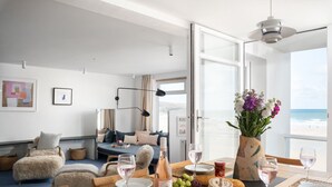 Ein modernes Wohnzimmer mit einer Couch, einem Esstisch gedeckt mit Weingläsern, einer Weinflasche und einer Blumenvase.