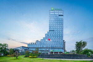 Un moderno hotel Holiday Inn con fachada de vidrio, un asta con banderas y un césped bien cuidado.