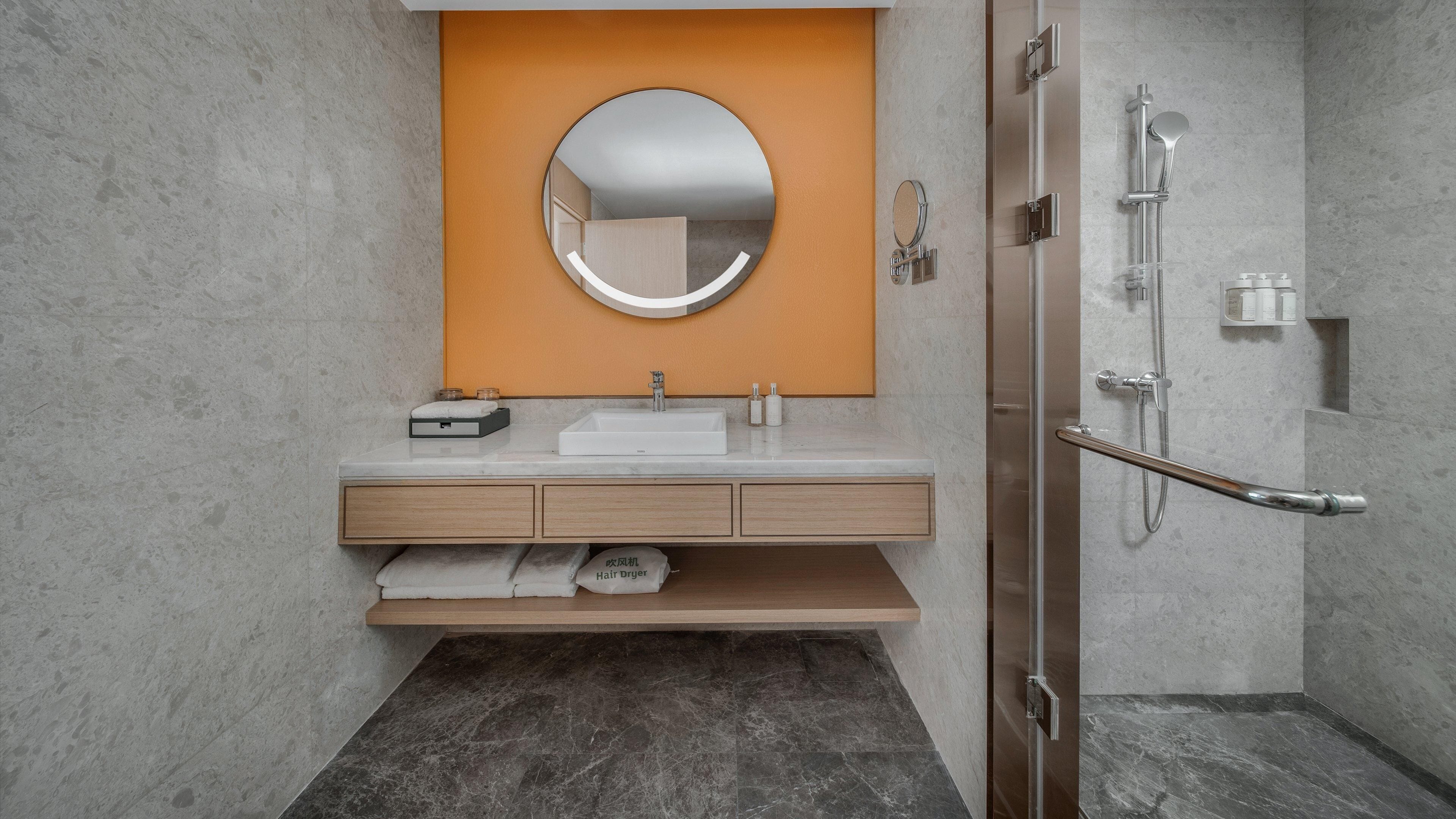 A modern bathroom with a marble sink, a round mirror, a towel rack, and a shower with a glass door.