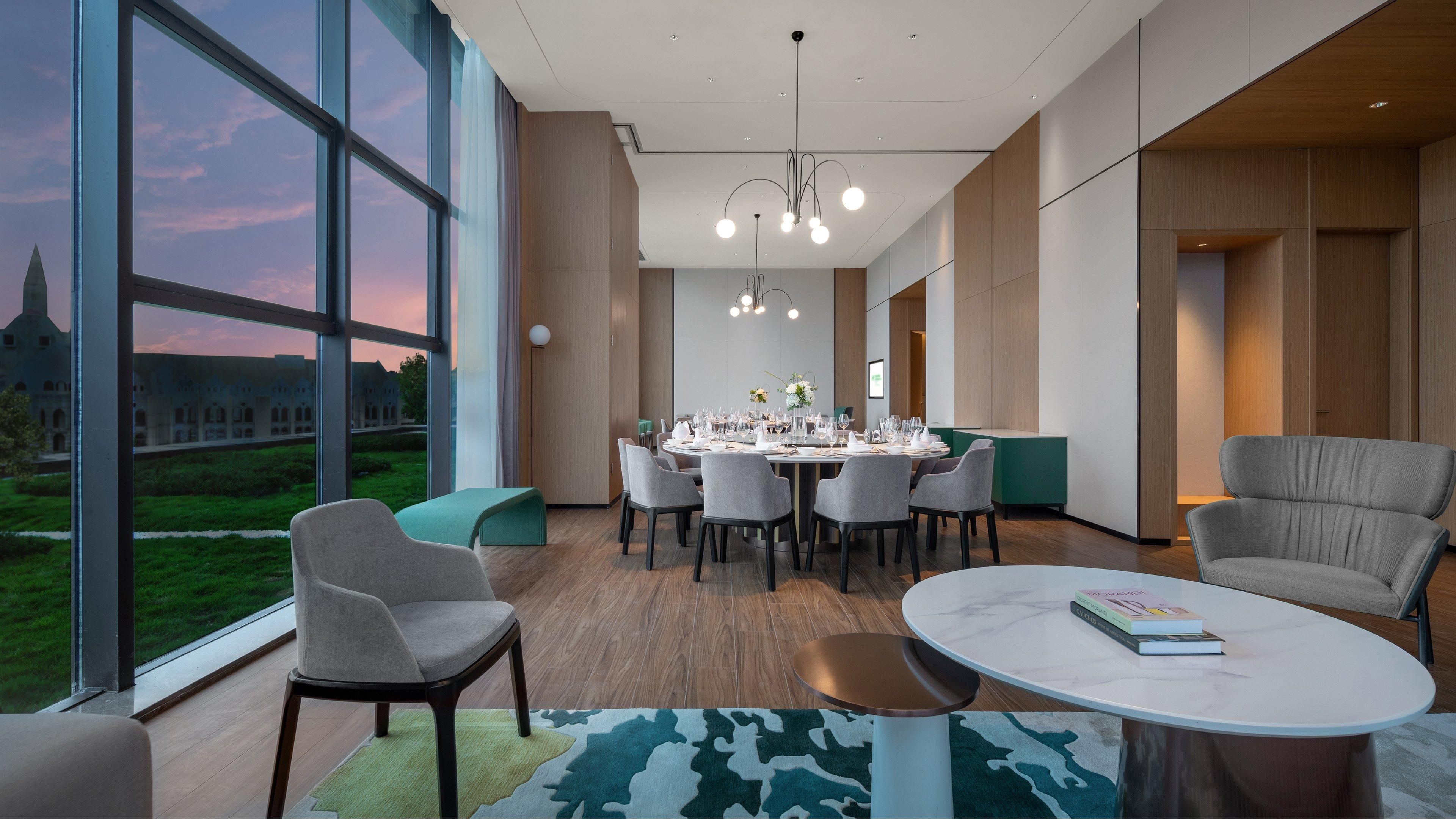 A modern dining area with a large table set for a meal, surrounded by chairs, and a view of a building through large windows.