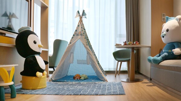 Zona infantil con una tienda de campaña, juguetes de peluche, una mesita con fruta y una silla.