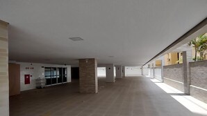 A spacious indoor area with a high ceiling, tiled floor, and a few pillars. - Edifício Promenade Apto 207-Mandi Hospit (Maceio)