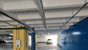 A parking garage with a blue wash station, a yellow pillar, and a white car in the background. - Edifício Promenade Apto 207-Mandi Hospit (Maceio)