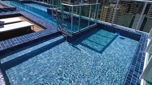 A rooftop swimming pool with clear blue water, surrounded by glass railings and a cityscape view. - Edifício Promenade Apto 207-Mandi Hospit (Maceio)