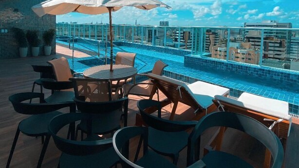 A rooftop pool area with lounge chairs and umbrellas, overlooking a cityscape. - Edifício Promenade Apto 207-Mandi Hospit (Maceio)