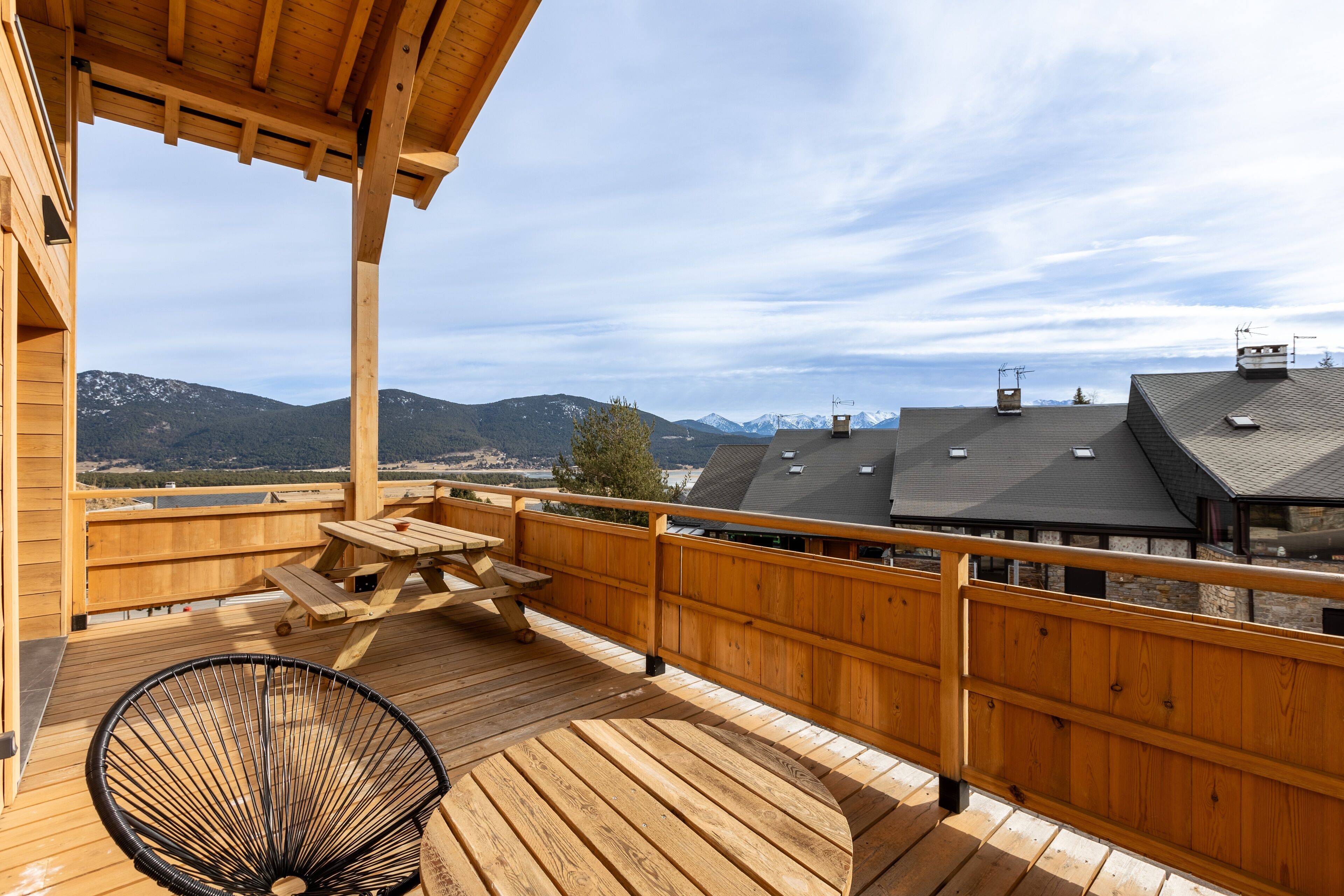 A wooden deck with a picnic table and a chair, overlooking a mountainous landscape.