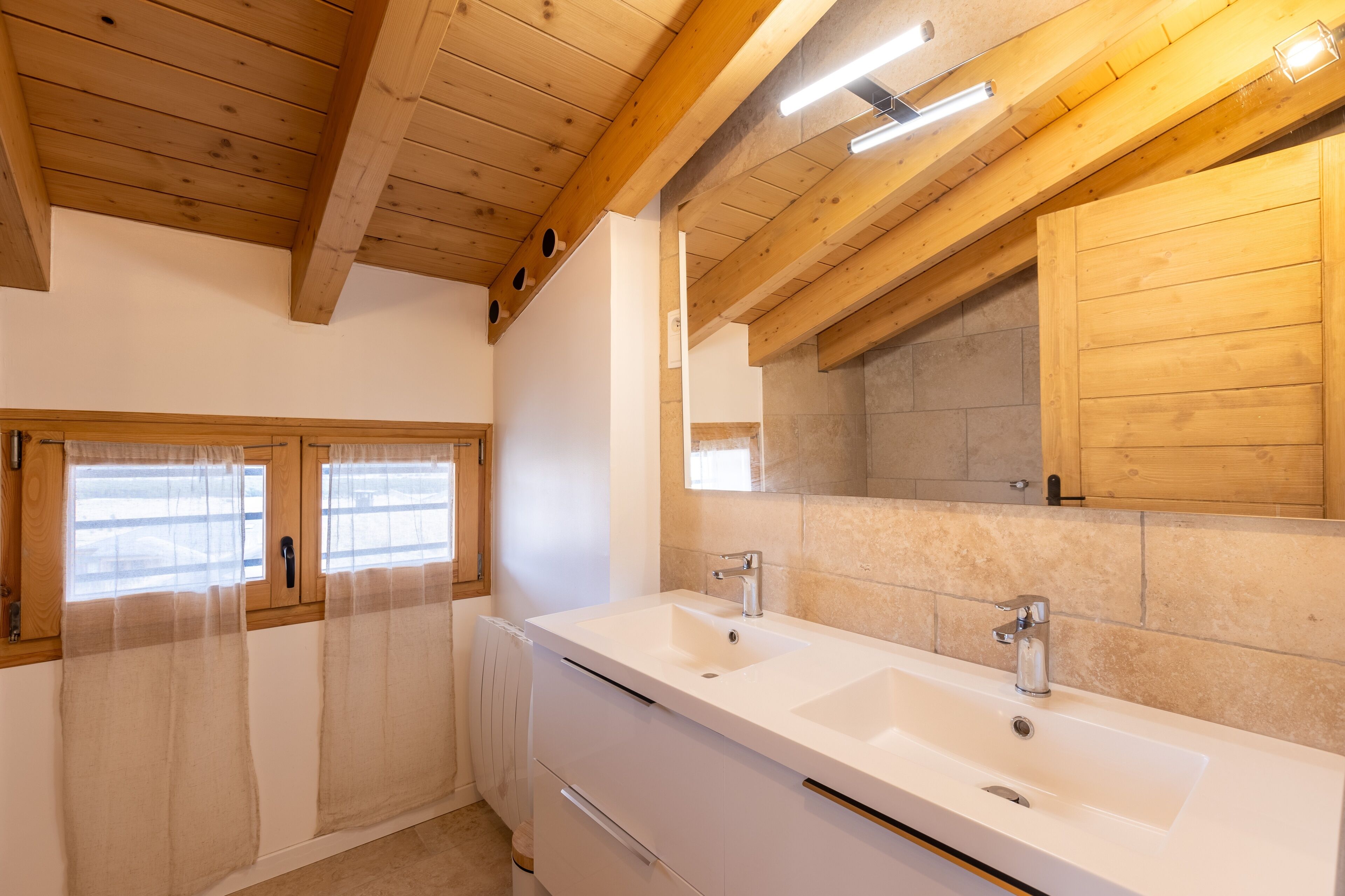 Une salle de bain avec des poutres en bois, un lavabo double et un miroir au-dessus du lavabo.