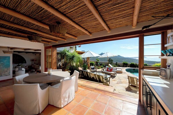 A spacious living area with a view of the sea, a pool, and outdoor furniture.