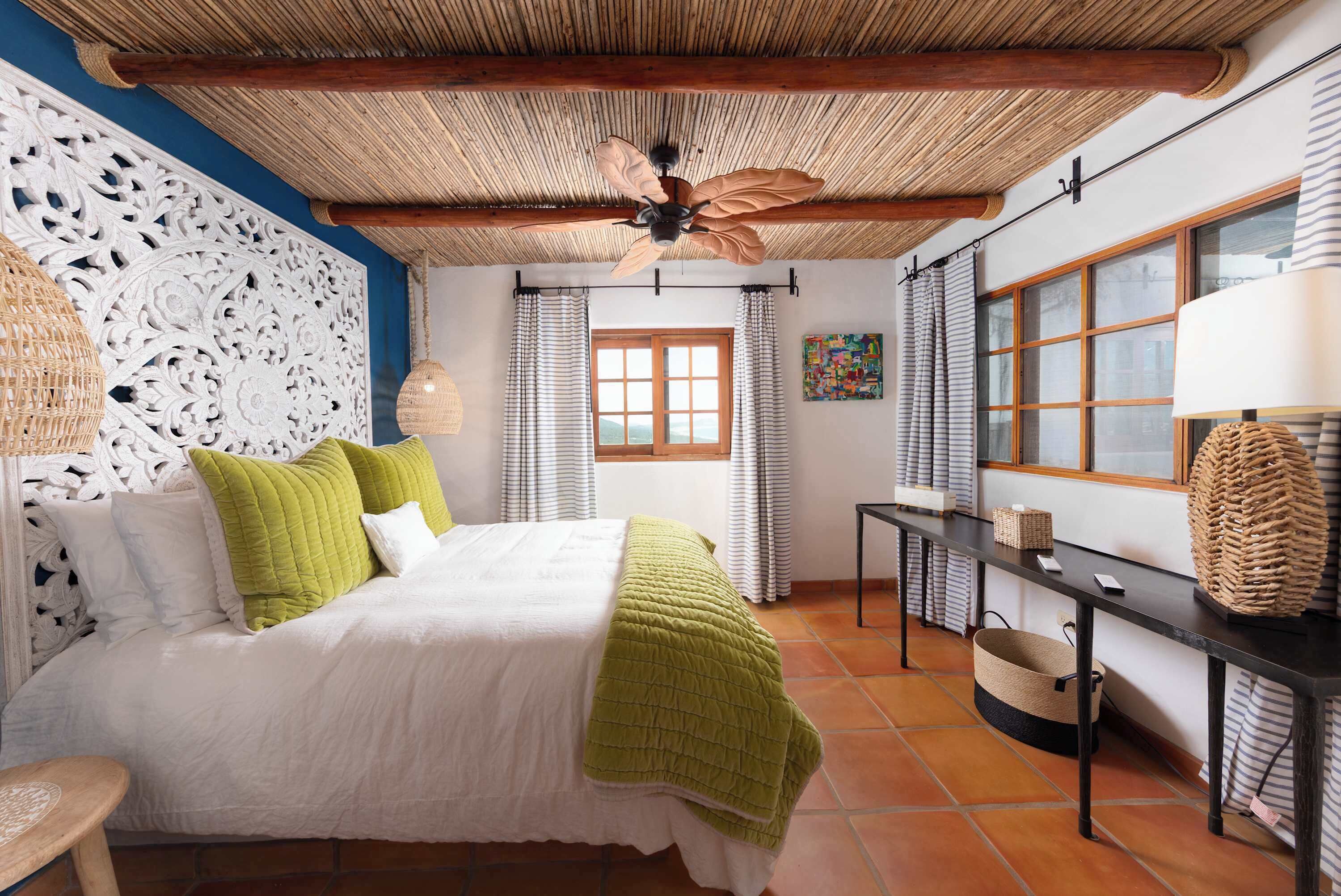 A bedroom with a bed, a ceiling fan, a window, and a table with a lamp.