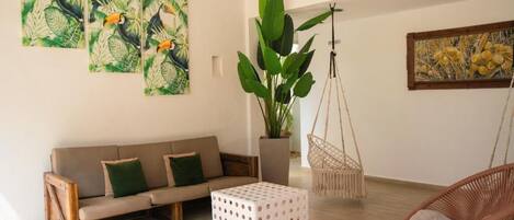 A modern living room with a sofa, a hanging chair, a potted plant, and artwork on the walls.