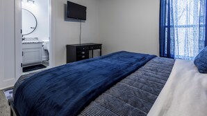 Un dormitorio con cama, cómoda, televisor y ventana con cortinas.