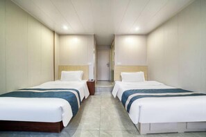 Habitación de hotel con dos camas, cabecera de madera, mesita de noche y una puerta que da a otra habitación.
